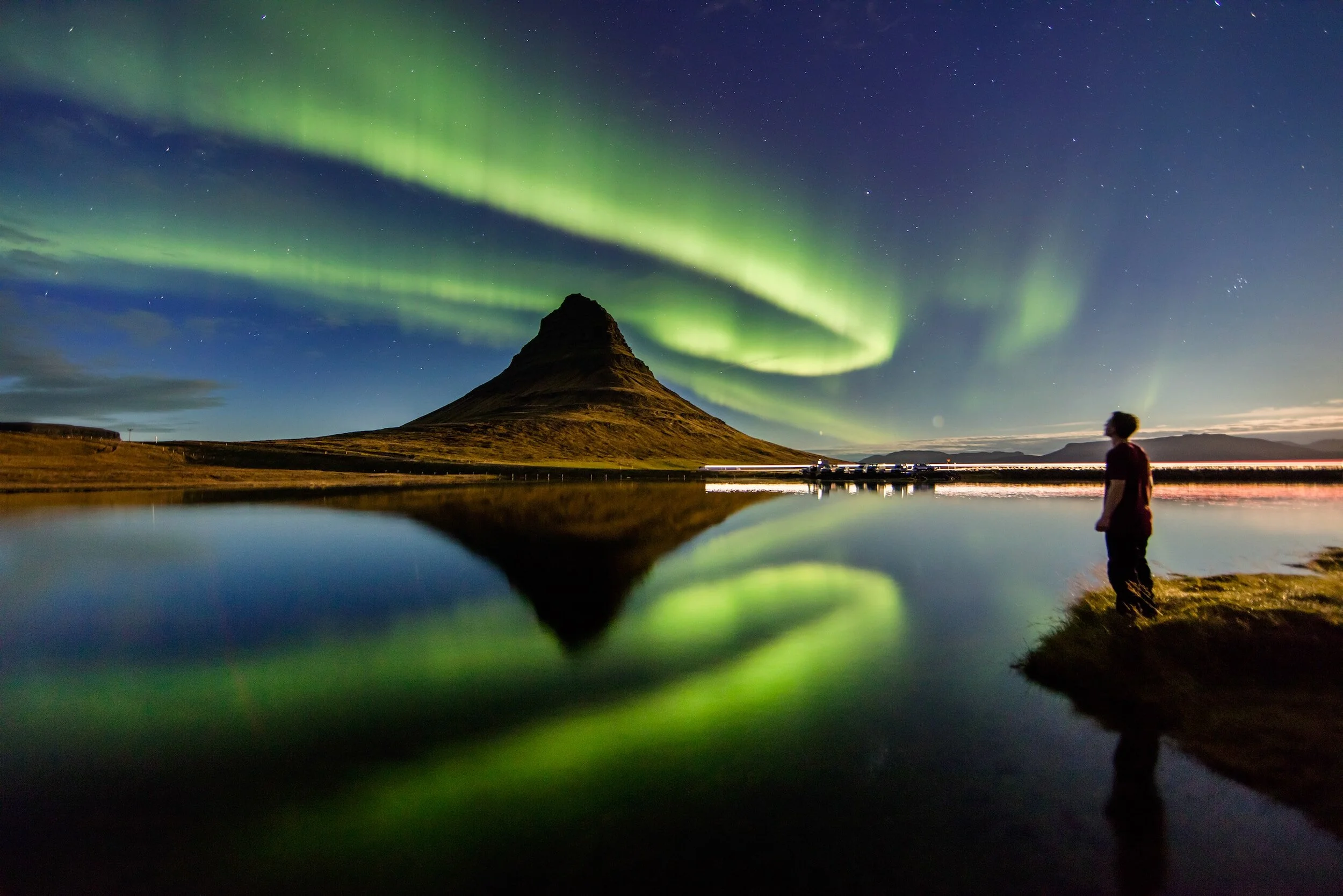 Man looks over lake toward northern lights in Iceland