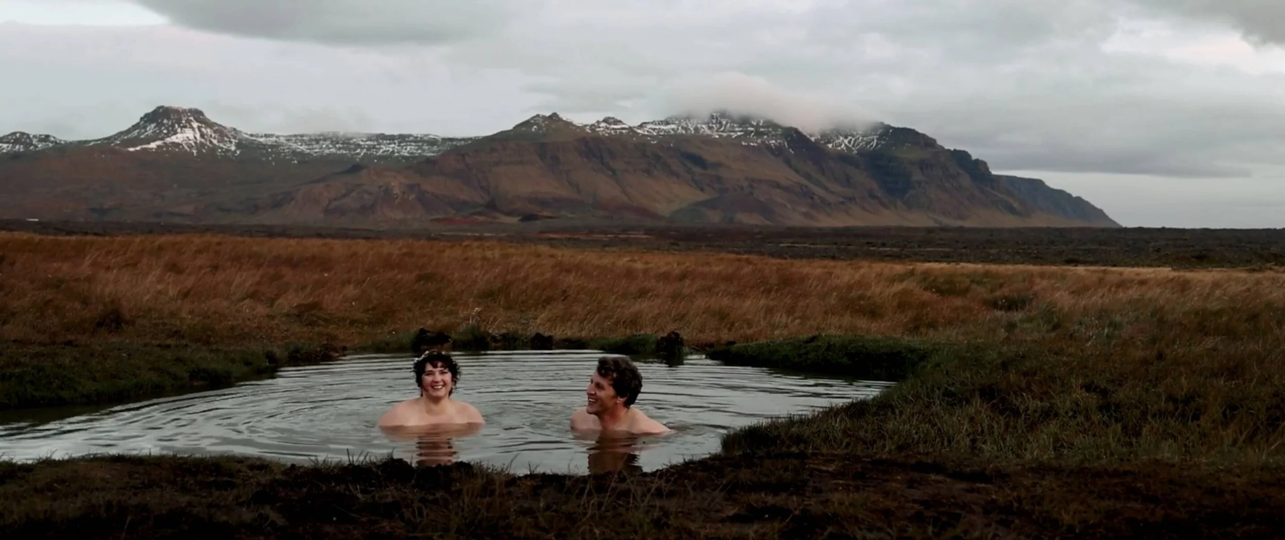 Iceland elopement couple bathe in hot springs with mountain background