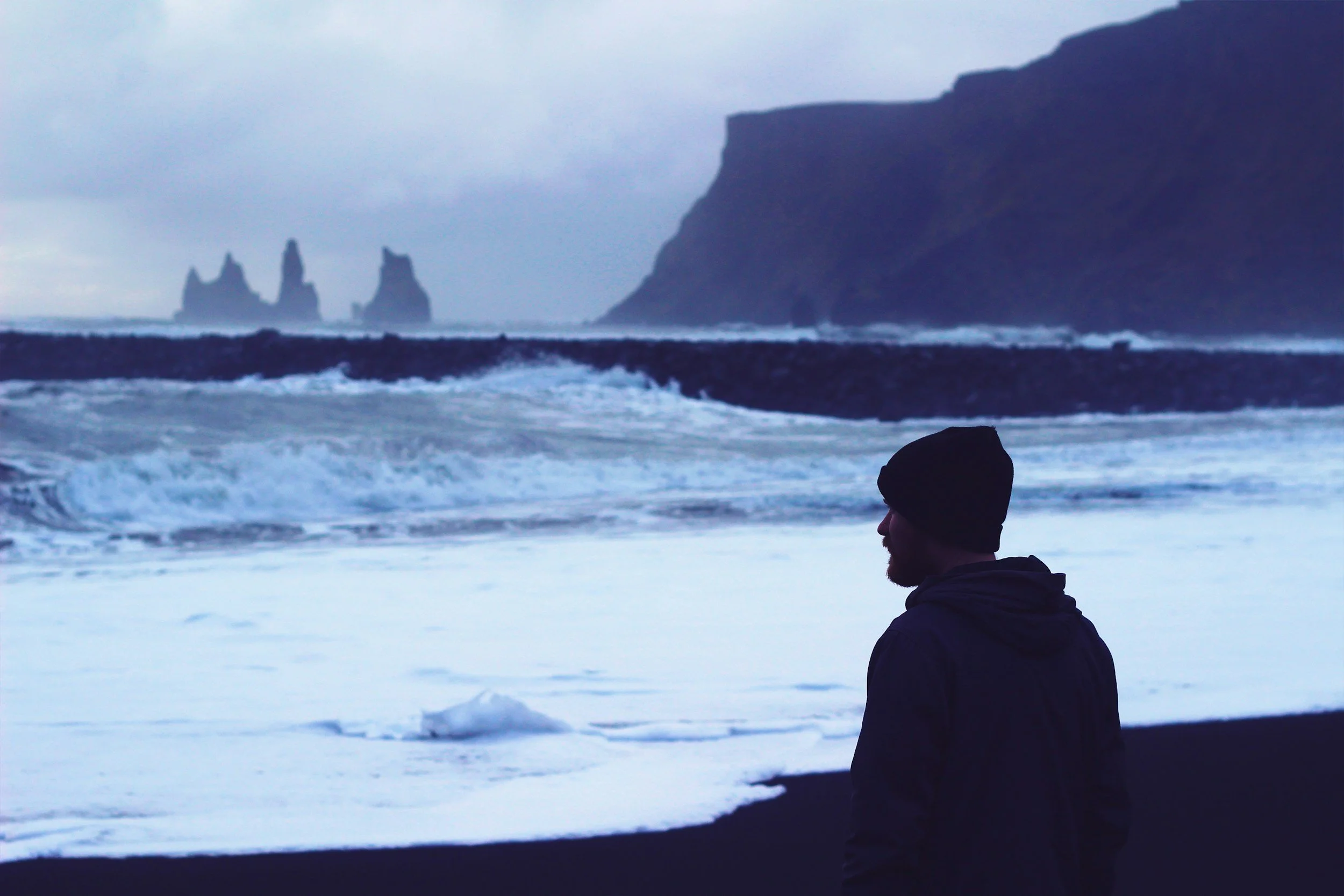 Bearded man looking out over a black sand beach in Iceland